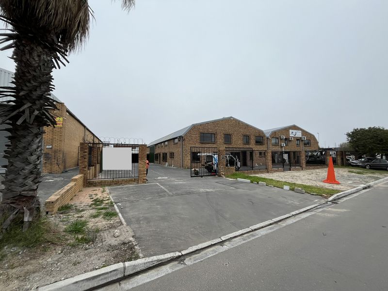 Industrial property featuring a brick facade, secure gated entrance, asphalt driveway, and wall-mounted air conditioning units.
