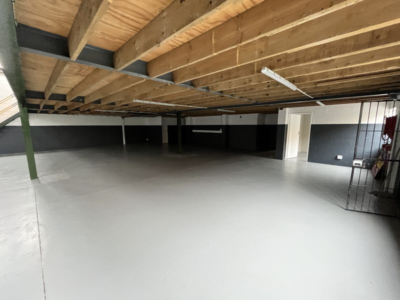 Spacious industrial utility area featuring exposed timber ceiling joists, painted concrete block walls, and a durable epoxy-coated concrete floor.