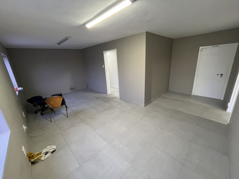 A spacious, empty office area featuring neutral wall tones, tiled flooring, and overhead fluorescent lighting, suitable for various industrial or commercial workspace configurations.