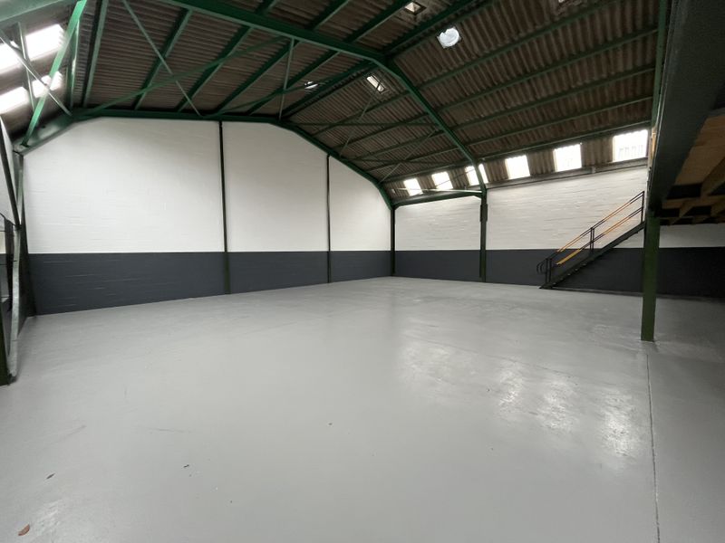 Spacious industrial warehouse unit featuring high ceilings with exposed steel trusses, painted concrete walls, durable epoxy flooring, and an integrated metal staircase.