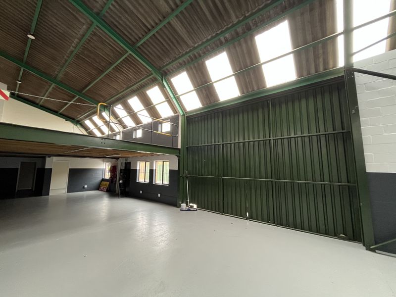 Spacious industrial utility area featuring a mezzanine level, high ceilings with translucent roof panels, and a large sliding access door.