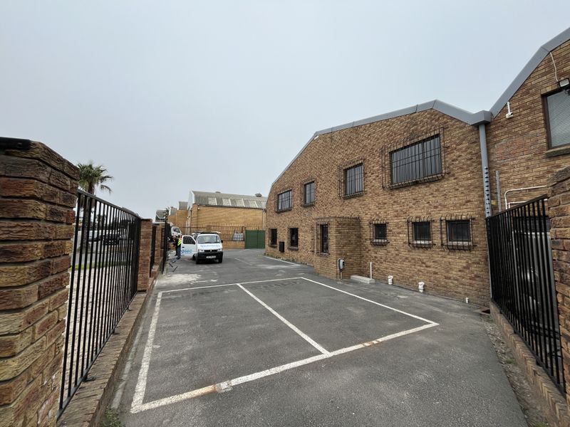 Exterior view of an industrial property featuring a face brick facade, secure perimeter fencing, and designated asphalt parking bays.