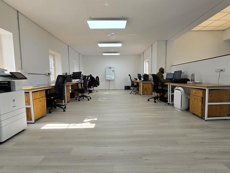 Spacious open-plan office area featuring modern laminate flooring, recessed LED lighting, and built-in wooden workstations with integrated electrical infrastructure.