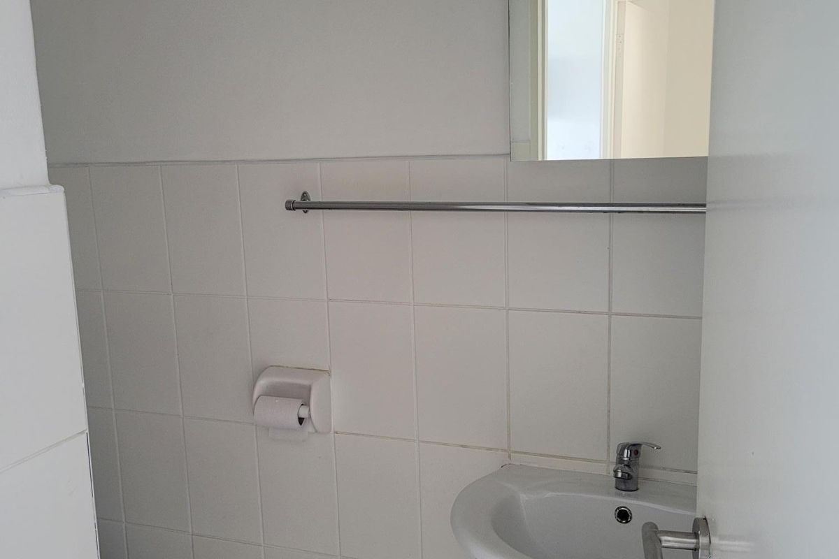 A compact office bathroom featuring a pedestal basin, chrome fixtures, and neutral ceramic tiling throughout.