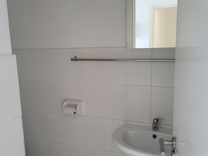A compact office bathroom featuring a pedestal basin, chrome fixtures, and neutral ceramic tiling throughout.