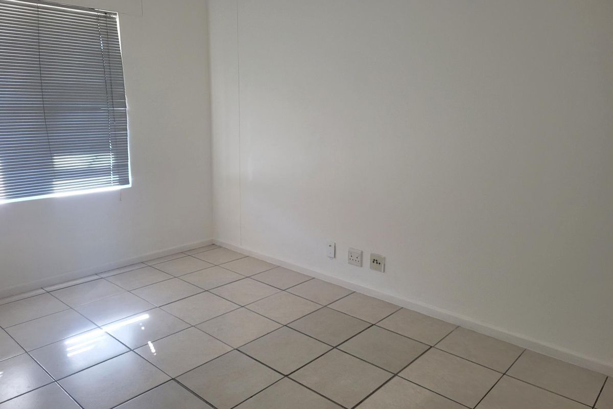 A clean, empty office space featuring neutral tiled flooring, white walls, and venetian blinds, equipped with integrated electrical and data connectivity points.