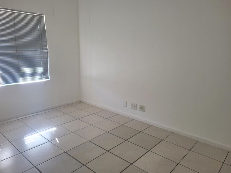 A clean, empty office space featuring neutral tiled flooring, white walls, and venetian blinds, equipped with integrated electrical and data connectivity points.