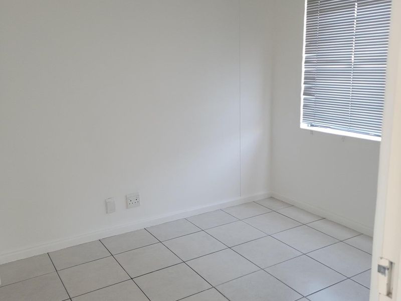 A clean, empty office space featuring neutral tiled flooring and fitted venetian blinds, providing a versatile environment for professional use.