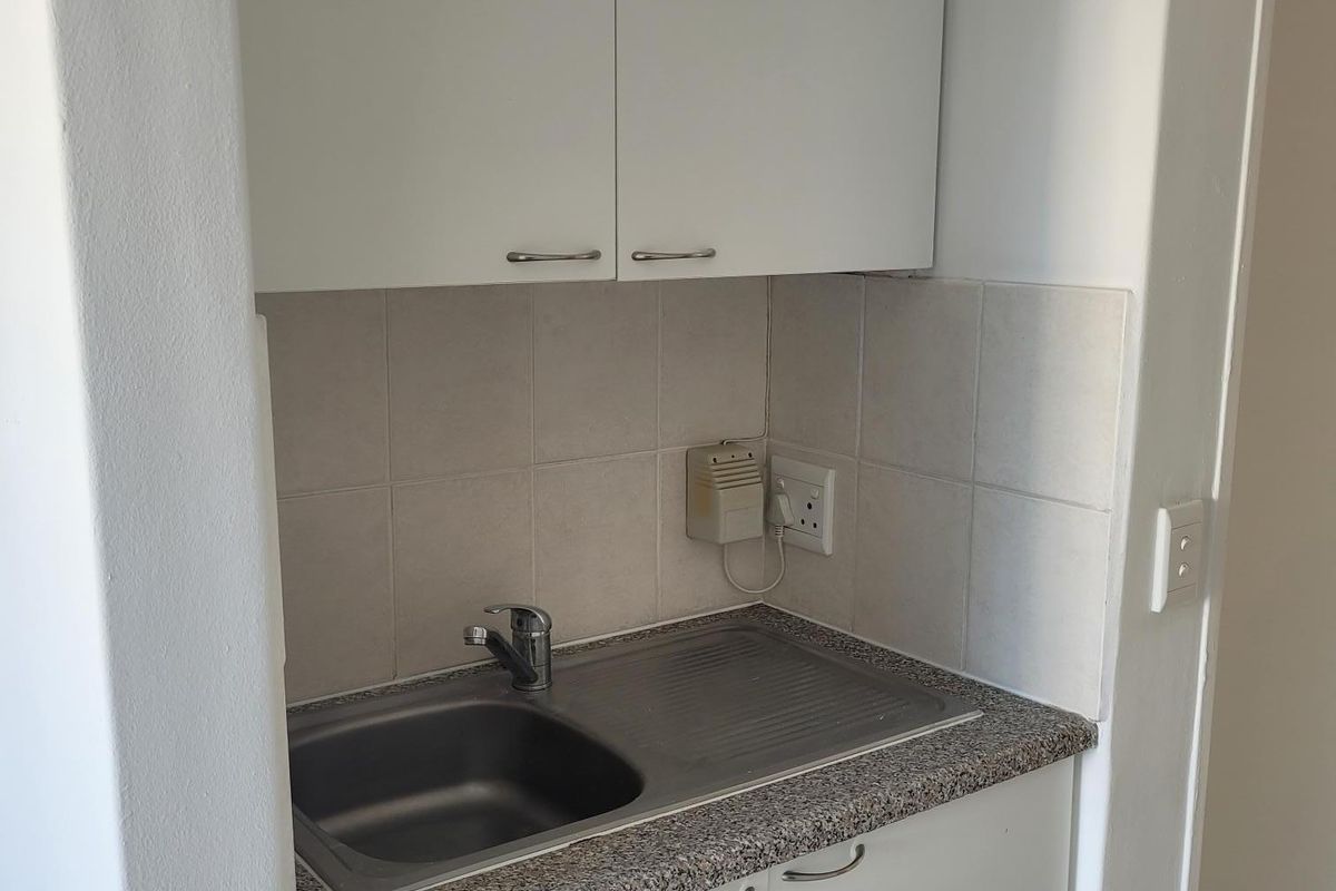 A compact scullery or kitchenette area featuring built-in white cabinetry, a stainless steel sink, and a durable laminate countertop with a tiled backsplash.