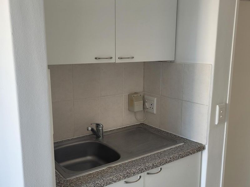 A compact scullery or kitchenette area featuring built-in white cabinetry, a stainless steel sink, and a durable laminate countertop with a tiled backsplash.