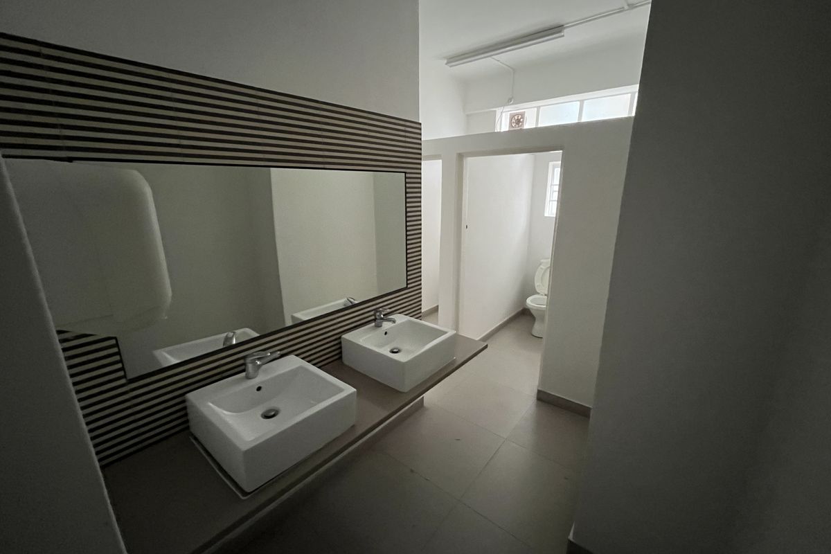 A clean, modern office bathroom featuring a double vanity with vessel sinks, a decorative slatted wood wall, and a separate toilet cubicle.