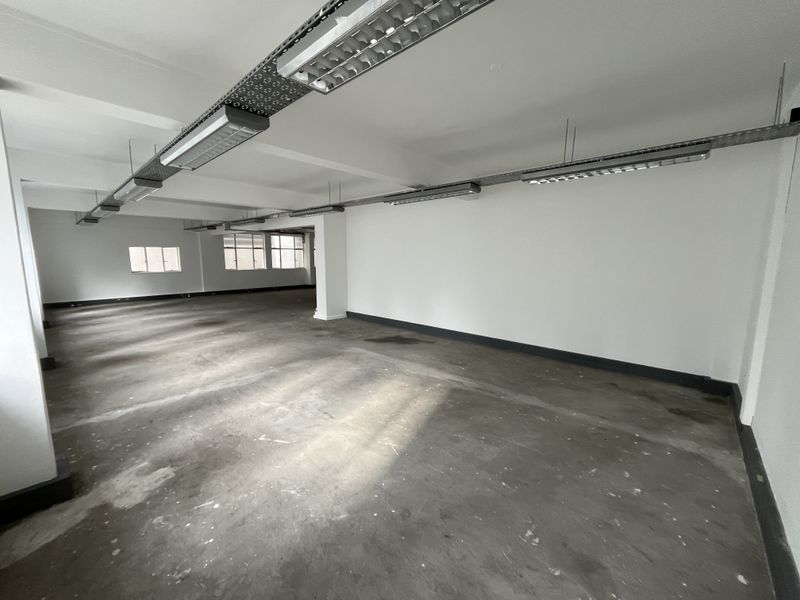 A spacious, open-plan office area featuring exposed industrial cable trays, fluorescent lighting, and unfinished concrete flooring, ready for custom fit-out.
