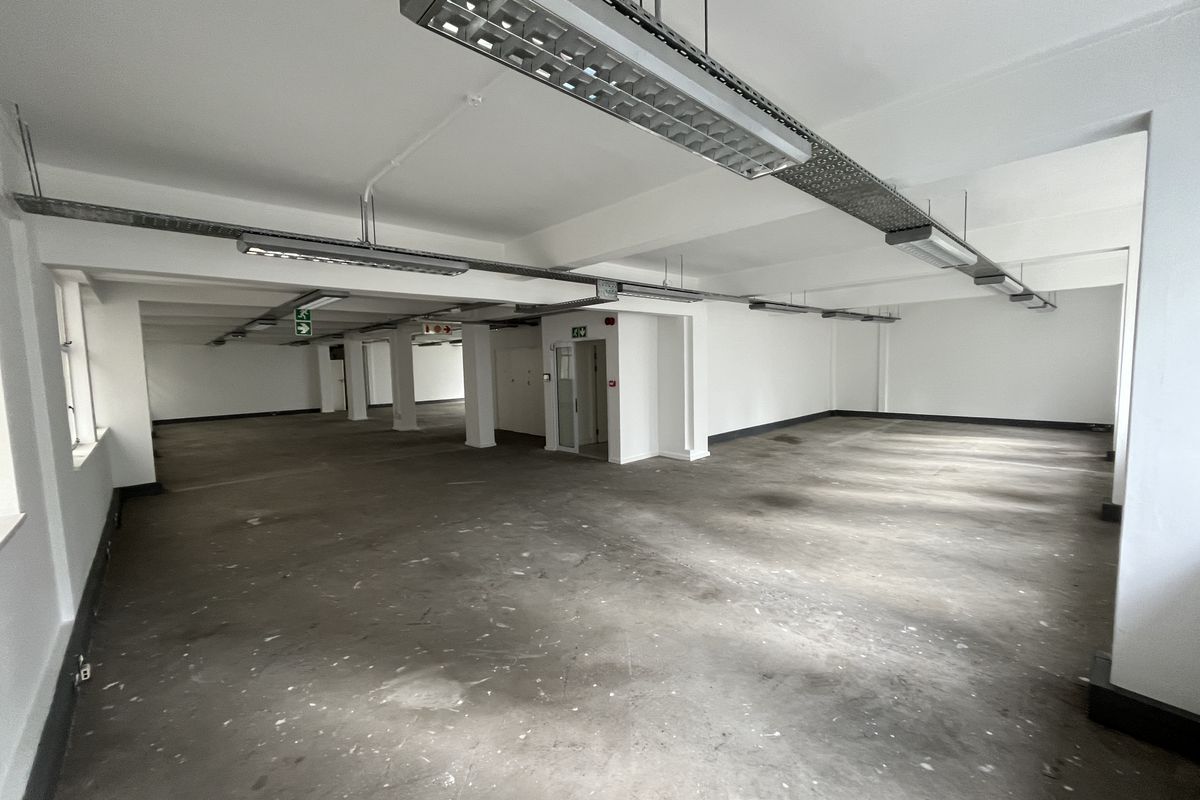 A spacious, open-plan office area featuring exposed cable trays, industrial lighting, and concrete flooring, offering a blank canvas for custom workspace configuration.