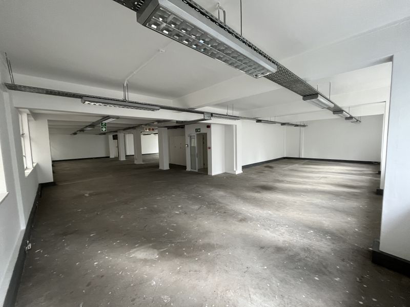 A spacious, open-plan office area featuring exposed cable trays, industrial lighting, and concrete flooring, offering a blank canvas for custom workspace configuration.