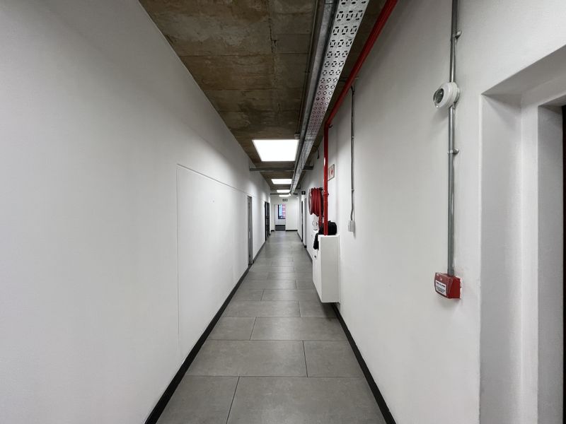A clean, modern office hallway featuring an exposed concrete ceiling, tiled flooring, and integrated fire safety infrastructure.