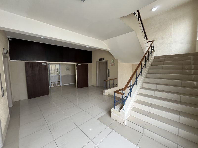 Spacious office building entrance lobby featuring tiled flooring, a central staircase with wooden handrails, and elevator access.