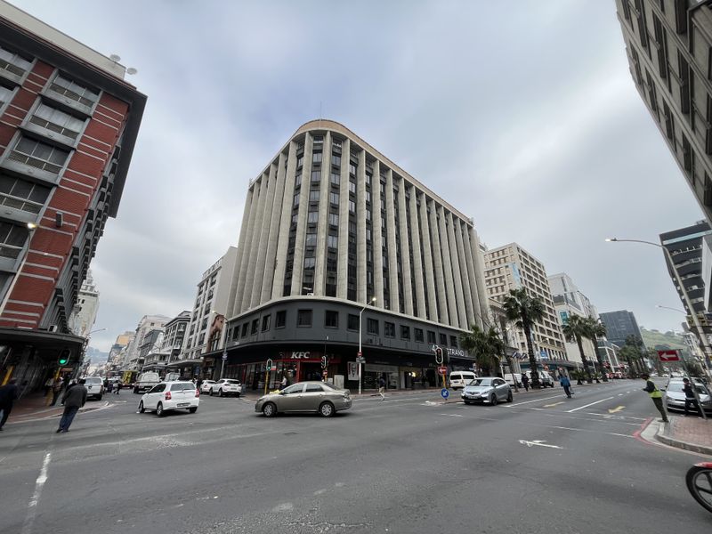 Street-level view of a multi-story commercial office building featuring a prominent curved corner facade and ground-floor retail space in a busy urban setting.