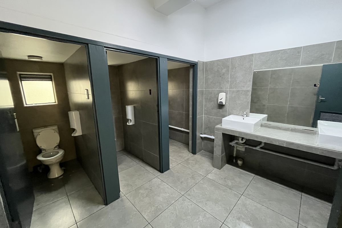 A functional office bathroom featuring tiled finishes, multiple toilet cubicles, and a built-in vanity with dual basins.
