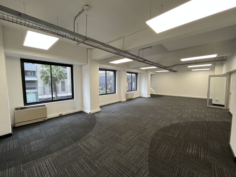 Spacious open-plan office area featuring large windows, suspended lighting, exposed industrial cable trays, and durable carpet tiles.