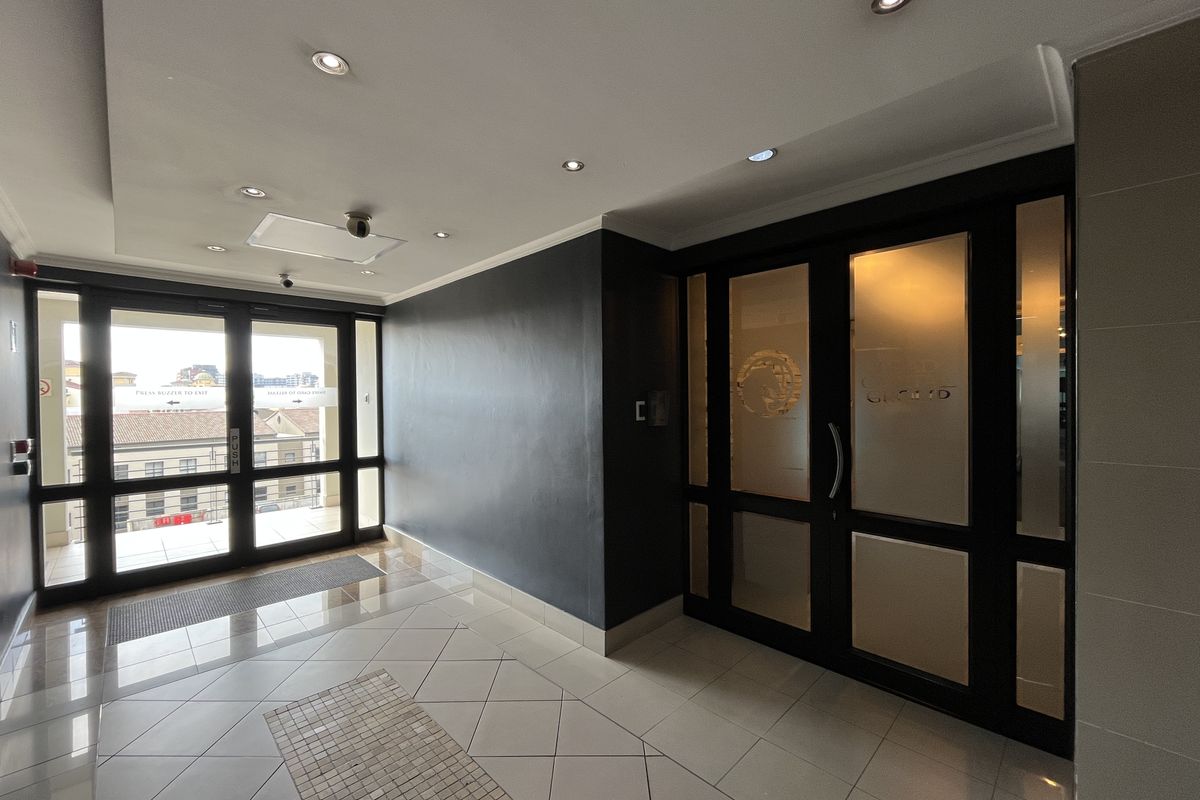 A clean and professional office building entrance lobby featuring tiled flooring, recessed lighting, and secure glass panel doors.