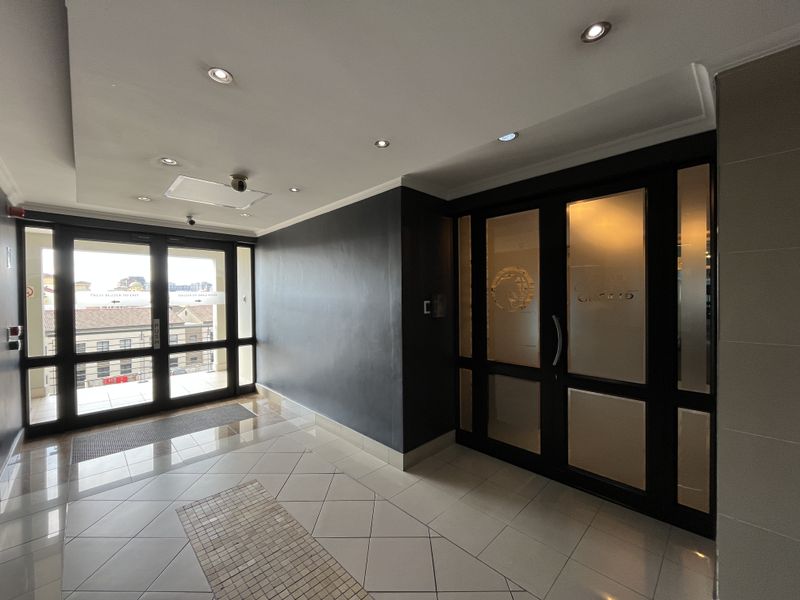 A clean and professional office building entrance lobby featuring tiled flooring, recessed lighting, and secure glass panel doors.