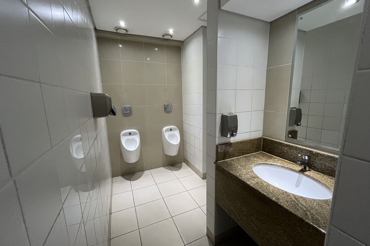 A clean, functional office restroom featuring two wall-mounted urinals, a vanity basin with a granite countertop, and tiled finishes throughout.