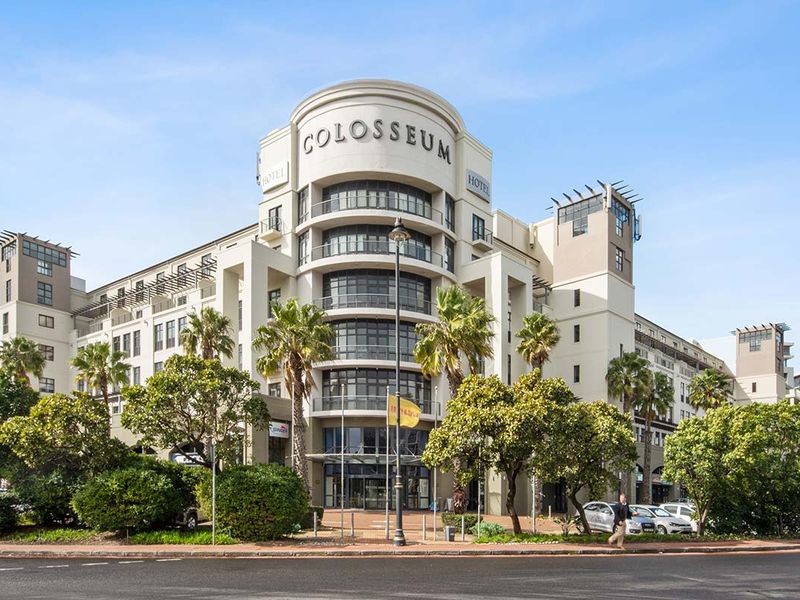 A professional exterior view of the Colosseum building, showcasing its prominent curved architectural design, multi-level balconies, and modern glass entrance.