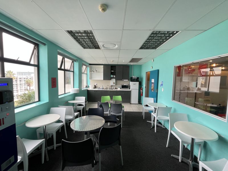 A functional office breakroom featuring a kitchenette with cabinetry, sink, and large windows providing natural light, suitable for staff use.