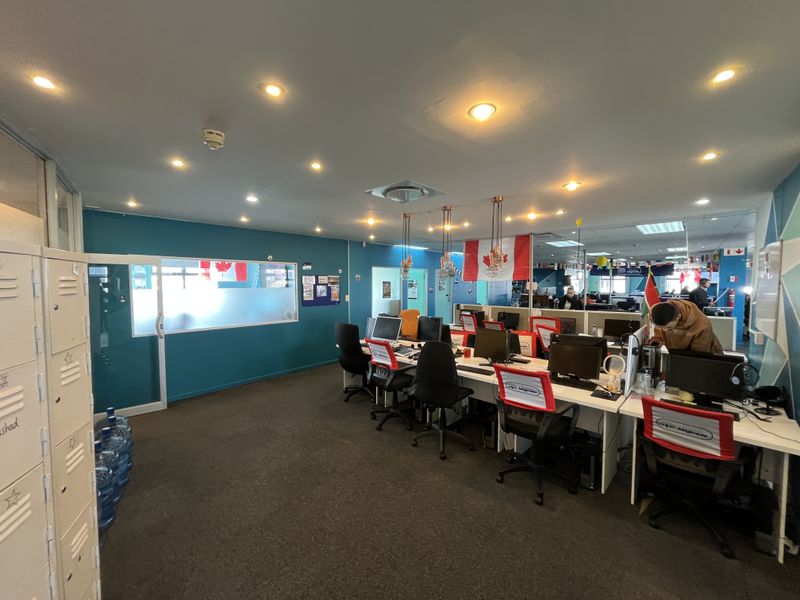 A functional open-plan office space featuring recessed lighting, carpeted flooring, and integrated metal storage lockers with glass partition walls.