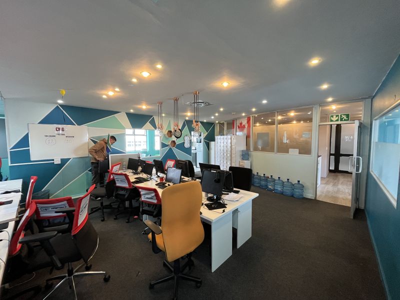 A functional open-plan office space featuring recessed ceiling lighting, glass partitioning, and modern geometric wall accents, providing a professional work environment.