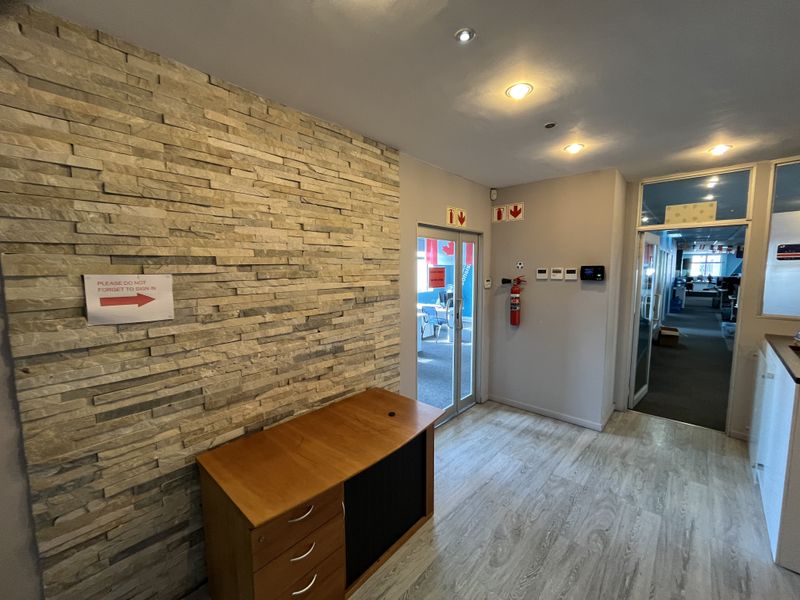 Office entrance area featuring a textured stacked stone feature wall, modern laminate flooring, and glass-paneled doors leading into the workspace.