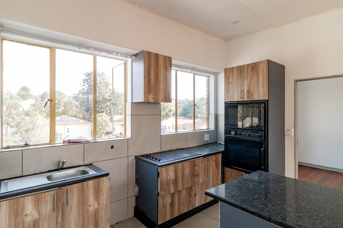 A functional kitchen featuring wood-look cabinetry, granite countertops, built-in oven and hob, and large windows providing ample natural light.