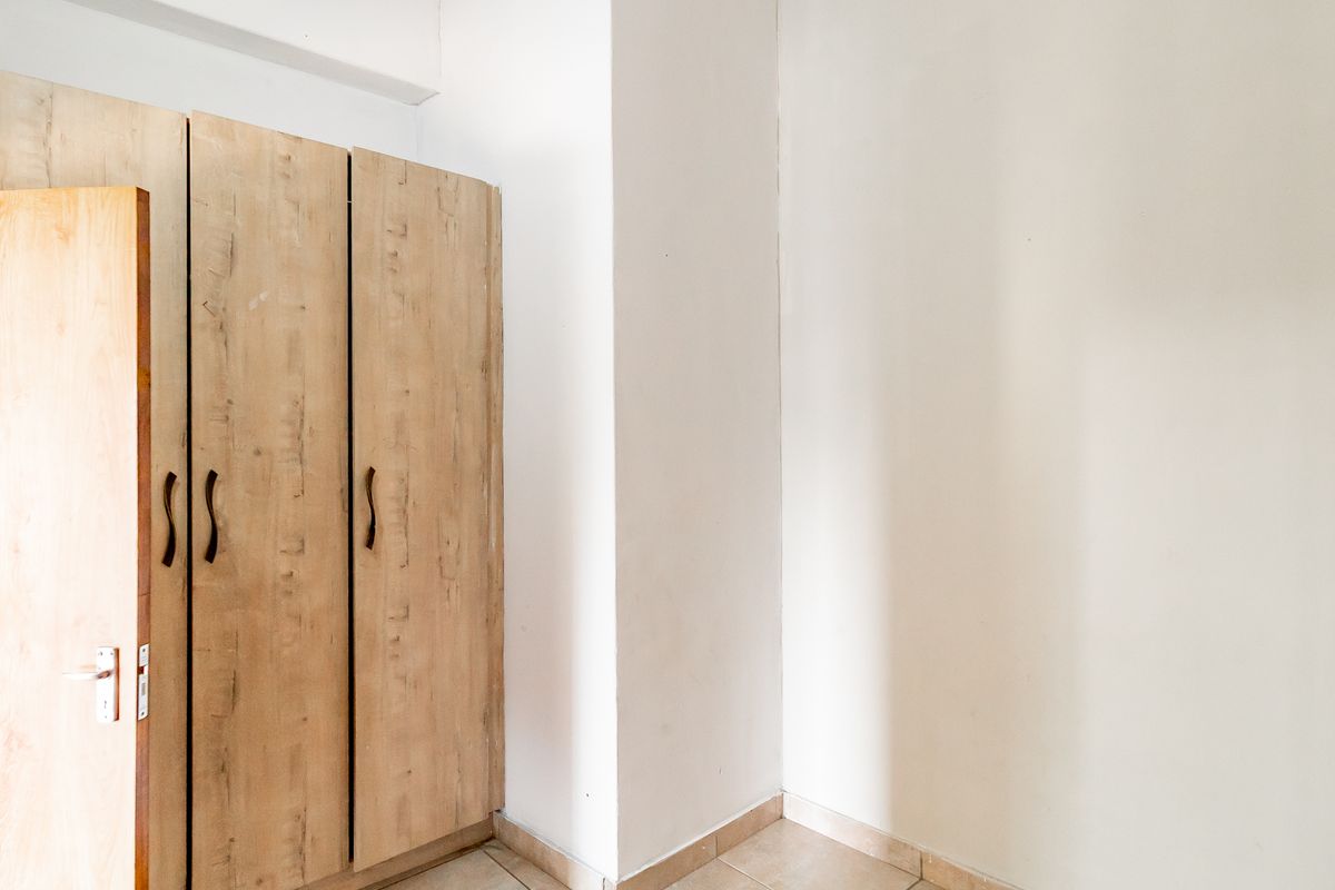 A clean, empty bedroom space featuring neutral tiled flooring and functional built-in wooden cupboards.