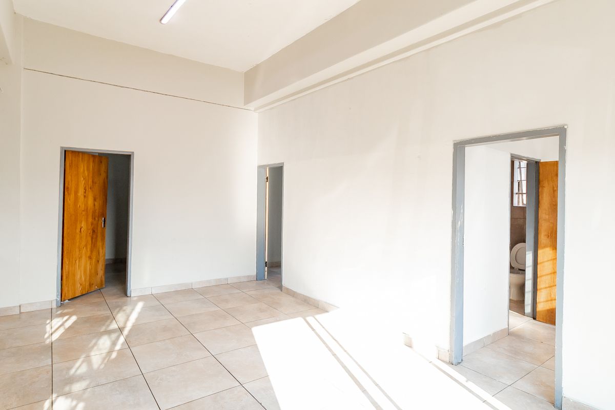 An empty, neutrally painted living area featuring tiled flooring and multiple doorways leading to adjacent rooms.