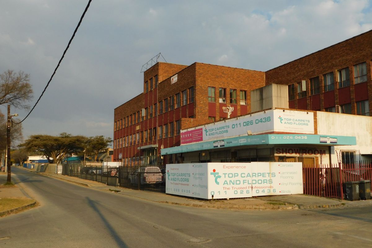 Street-level view of a multi-story commercial brick building featuring prominent signage and secure perimeter fencing.