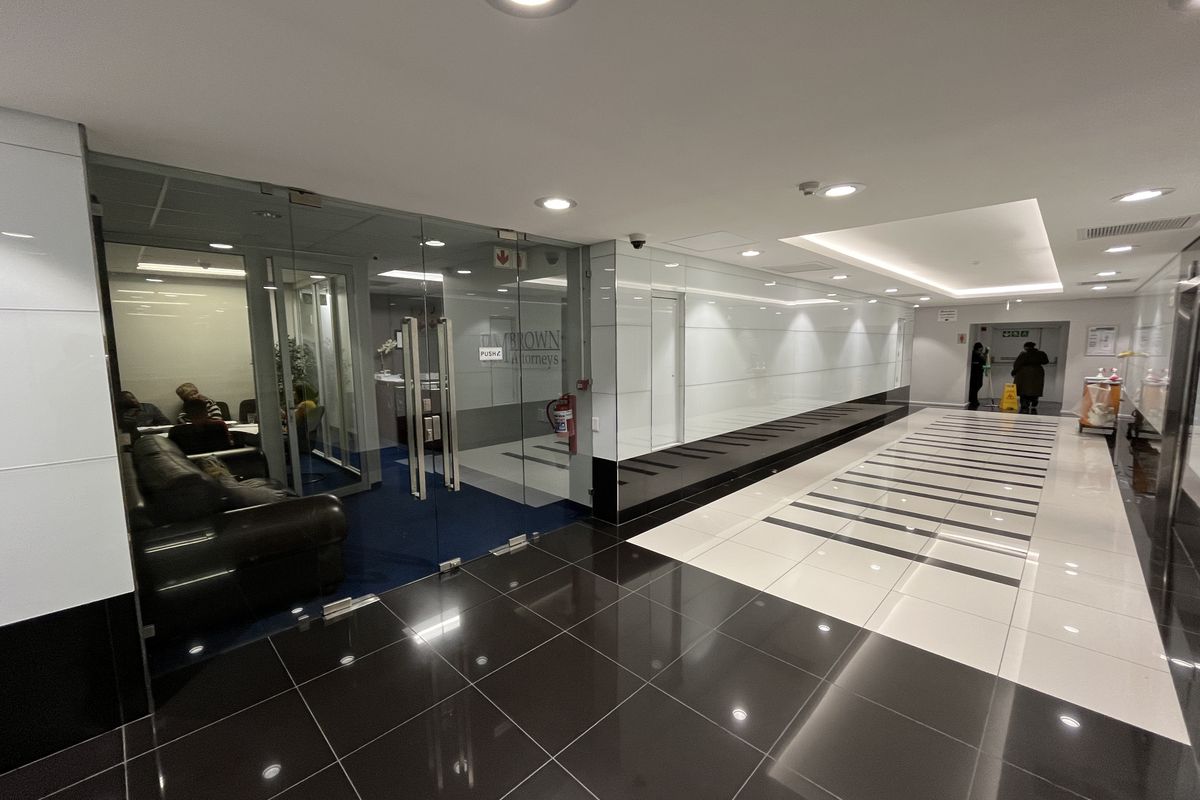 Modern office entrance lobby featuring glass partitions, high-gloss tiled flooring, and recessed ceiling lighting in a professional corporate setting.