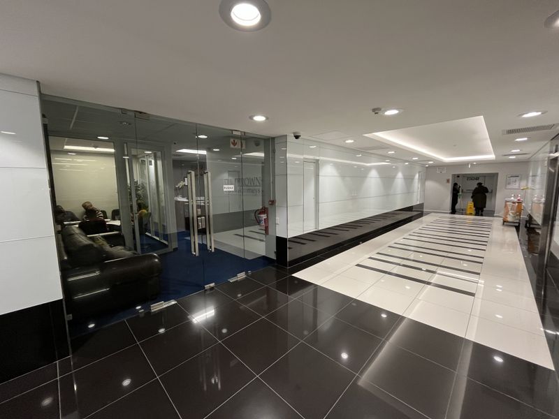 Modern office entrance lobby featuring glass partitions, high-gloss tiled flooring, and recessed ceiling lighting in a professional corporate setting.