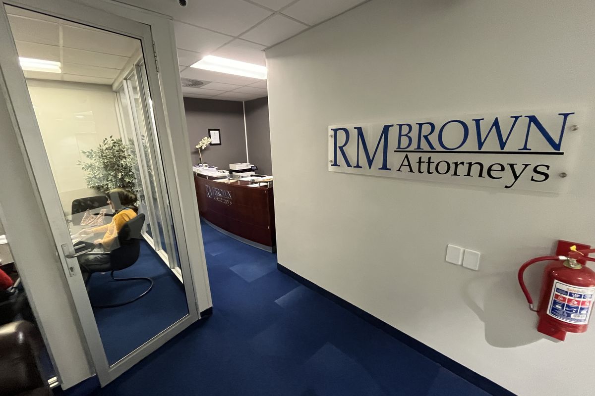 Professional office interior featuring a glass-partitioned meeting room, reception area, blue carpeting, and branded wall signage.