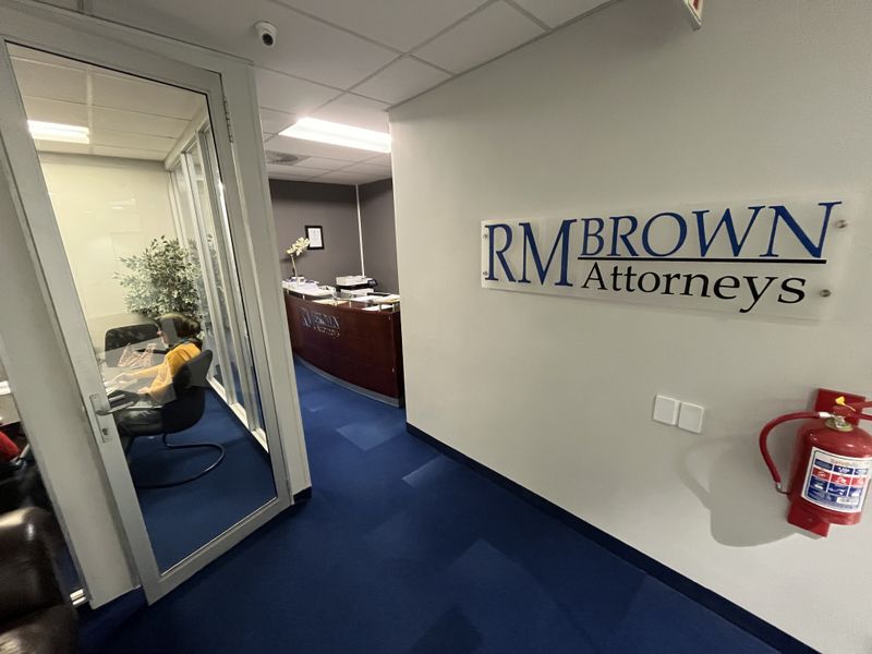 Professional office interior featuring a glass-partitioned meeting room, reception area, blue carpeting, and branded wall signage.