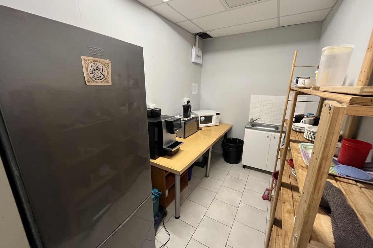 A functional office kitchenette featuring tiled flooring, a small sink with a tiled backsplash, and ample counter space for appliances.