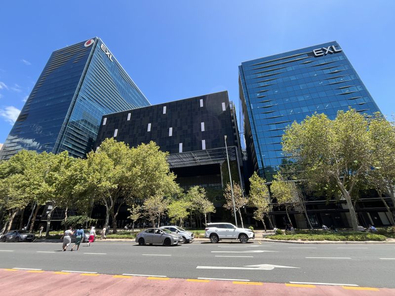 A modern multi-story office complex featuring glass curtain walls and a central dark-clad structure, situated along a tree-lined street.