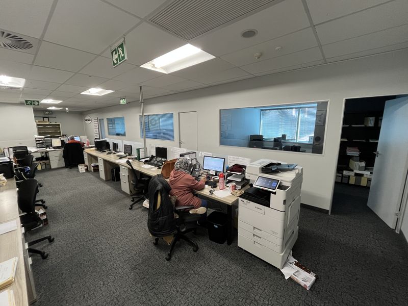 A functional open-plan office space featuring carpeted flooring, suspended ceilings with recessed lighting, and internal glass partitions for partitioned work areas.