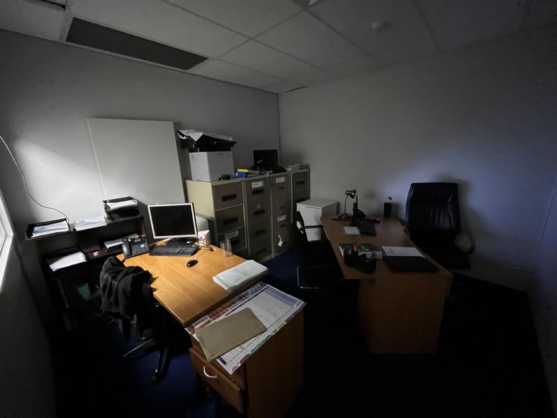 A functional office space featuring a suspended ceiling and carpeted flooring, currently set up with multiple workstations and storage cabinets.