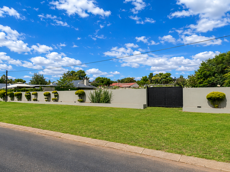 Street view of the restaurant property featuring a well-maintained perimeter wall, gated entrance, and manicured lawn area.