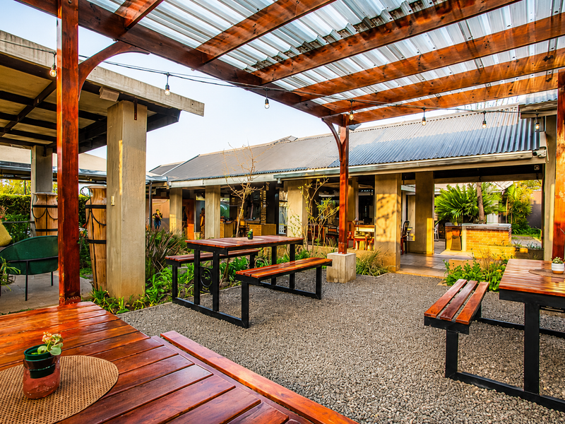 A spacious outdoor patio area featuring a timber pergola with corrugated roofing, concrete columns, and gravel flooring, ideal for restaurant dining.