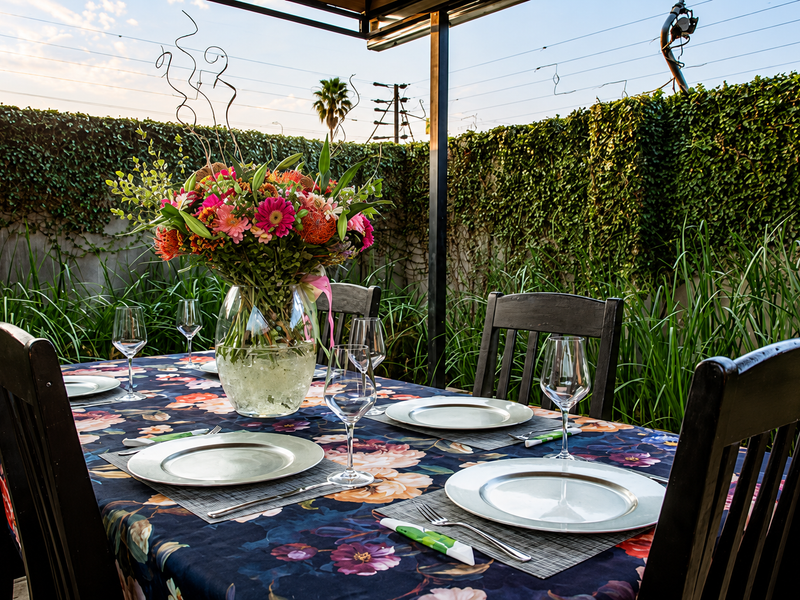 An inviting outdoor dining area on a covered patio, featuring a lush ivy-covered wall and a well-maintained setting.
