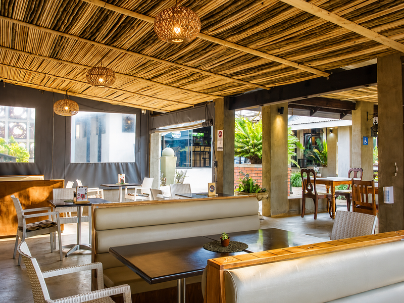 A covered outdoor dining area featuring a rustic bamboo ceiling, concrete support columns, and built-in booth seating, providing a comfortable and shaded restaurant space.
