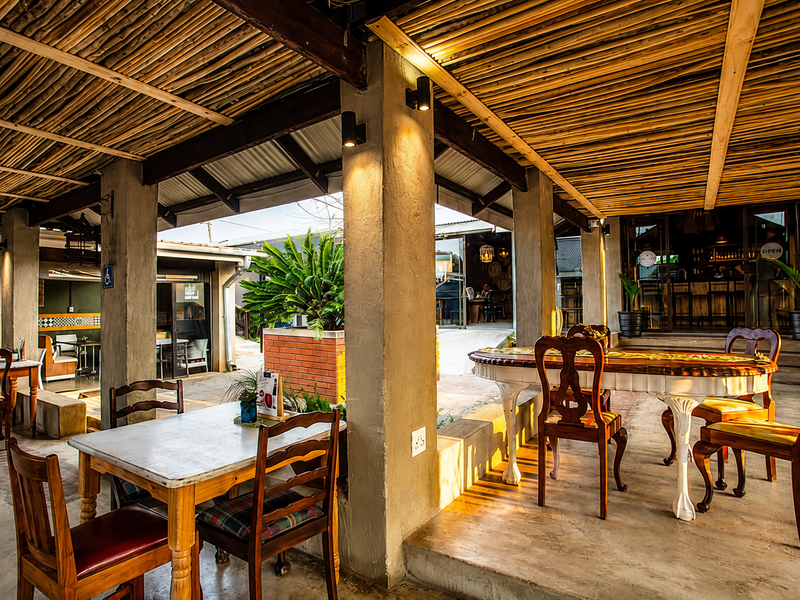 A covered outdoor dining area featuring a rustic bamboo ceiling, concrete pillars, and polished concrete flooring, providing a spacious and inviting atmosphere.