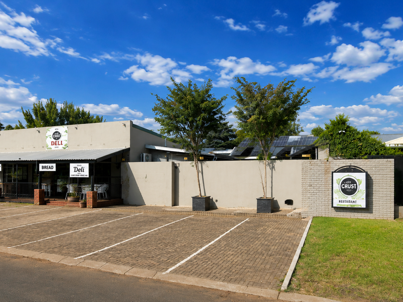 Front exterior view of the restaurant property featuring a paved parking area, covered patio entrance, and well-maintained boundary walls.