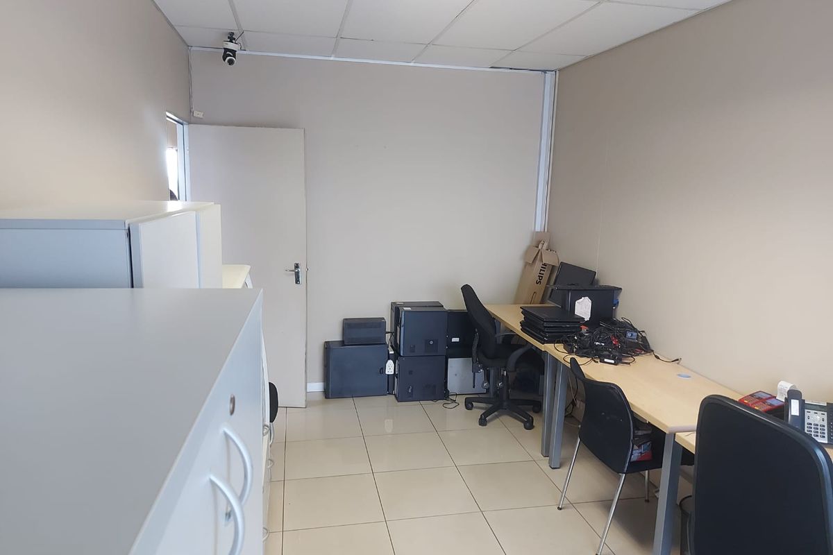 A functional office space featuring ceramic floor tiles, a suspended ceiling, and integrated security camera, suitable for a professional work environment.